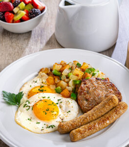 A breakfast place setting featuring fresh eggs, hash, and Al Fresco Chicken Sausages as links and patties