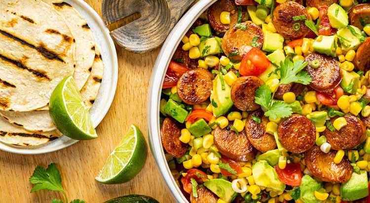 A fresh bowl of Al Fresco Rotisserie Chicken Sausage with corn avocado salad and fresh tortillas and lime