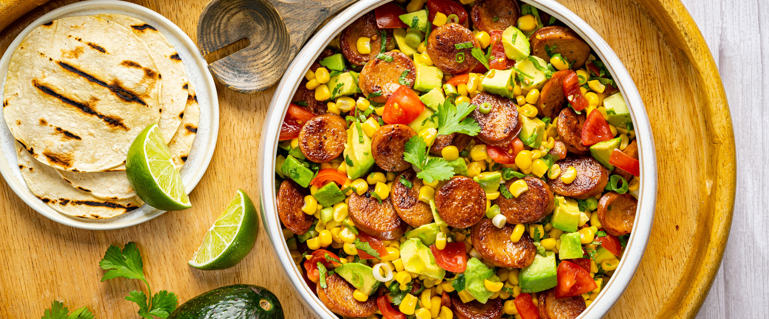A fresh bowl of Al Fresco Rotisserie Chicken Sausage with corn avocado salad and fresh tortillas and lime