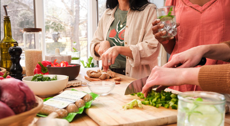 Hands chopping fresh ingredients and Al Fresco chicken sausage for a dish