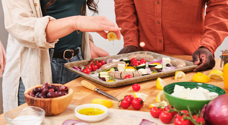 Man and woman squeezing lemon onto an Al Fresco chicken sausage sheet pan