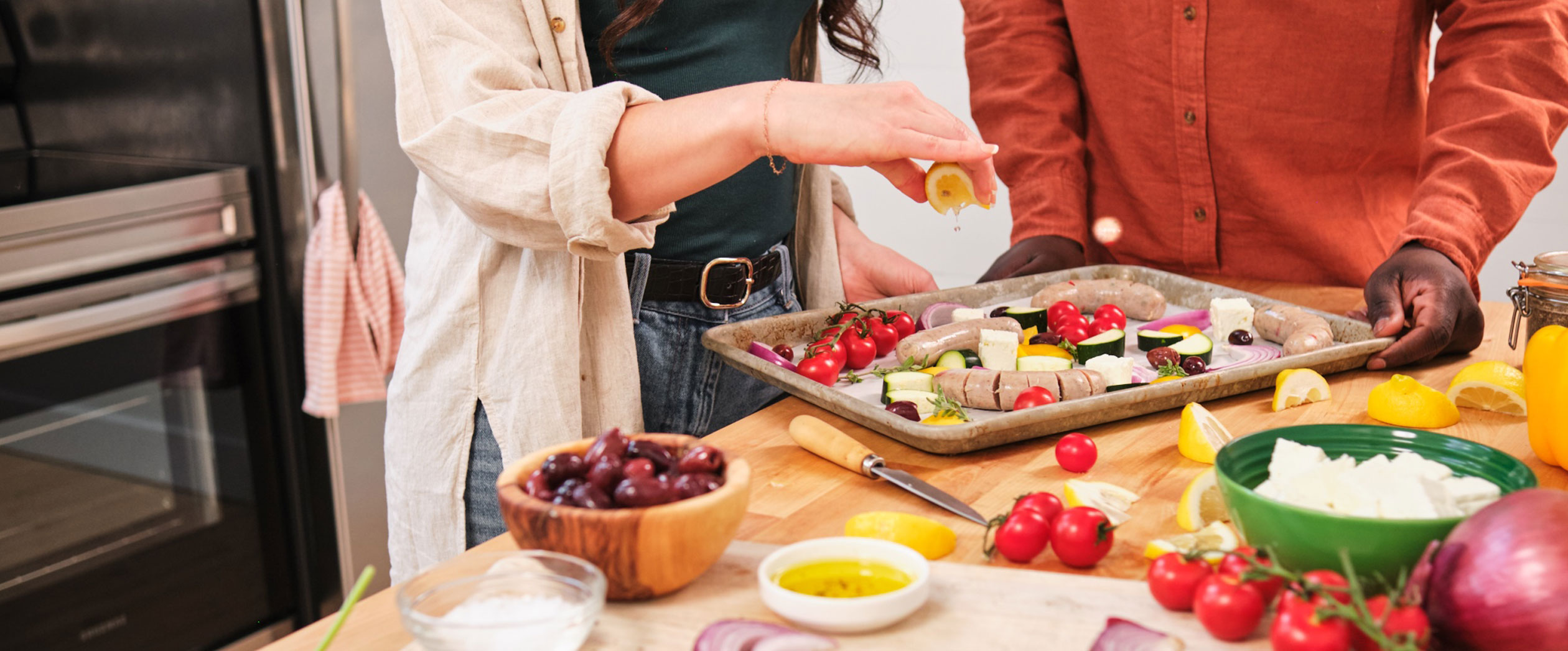 Man and woman squeezing lemon onto an Al Fresco chicken sausage sheet pan